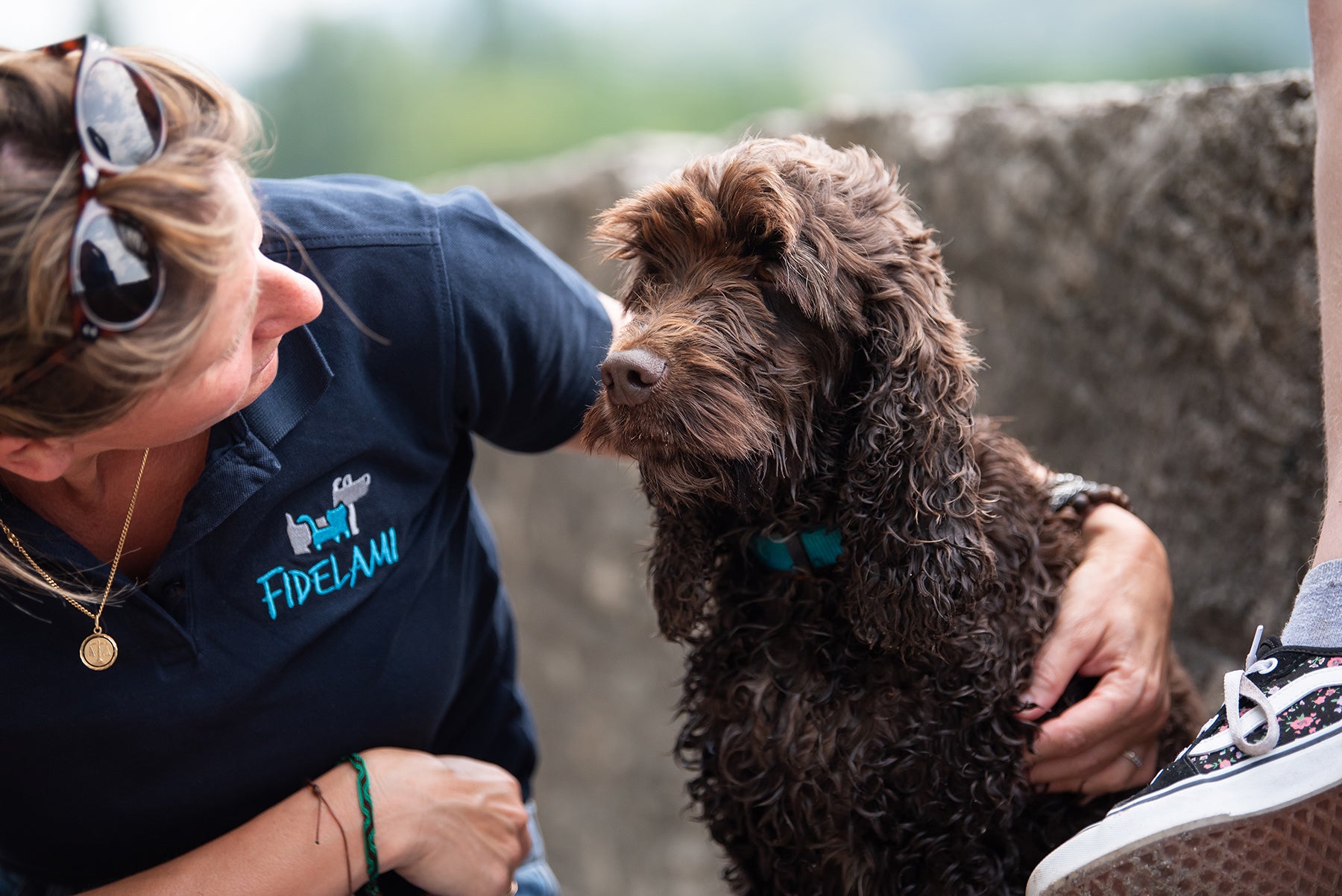 Femme blonde de l'équipe Fidelami en train de faire un câlin à un chien portant le collier PREMIUM bleu Fidelami. Ils se regardent avec amour, le chien est heureux et épanoui. Fidelami veille à votre bonheur à chaque instant : balade, jeux, voyages, repas, toilettage